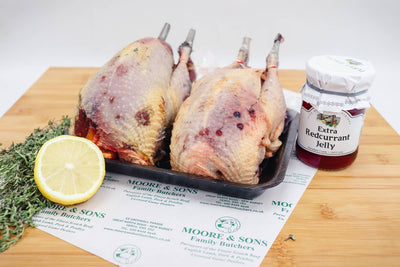 two pheasants on a butchers block with lemon, herbs and extra redcurrant jelly on the side